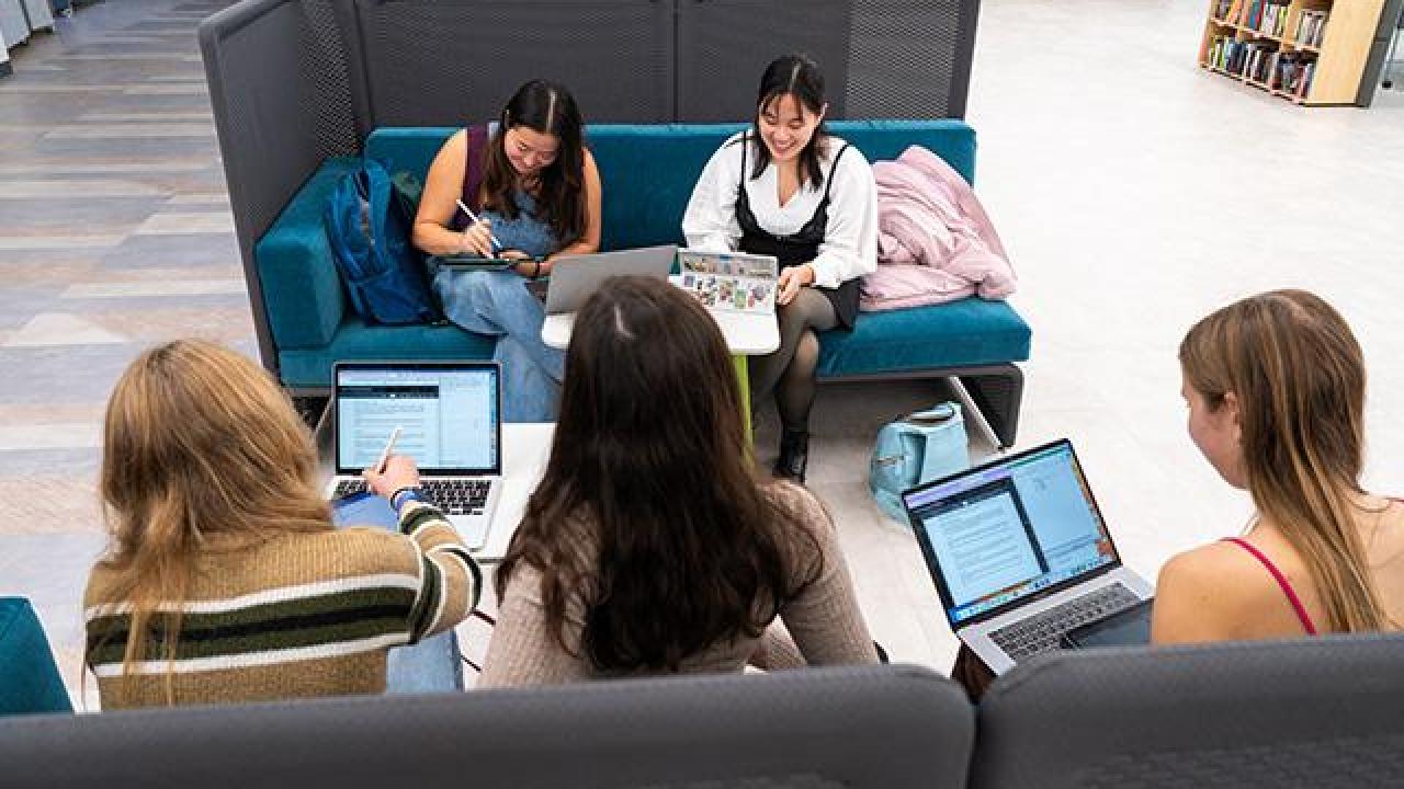 A photo taking from above looking down on a group of five students working in a booth in the Writing Center.