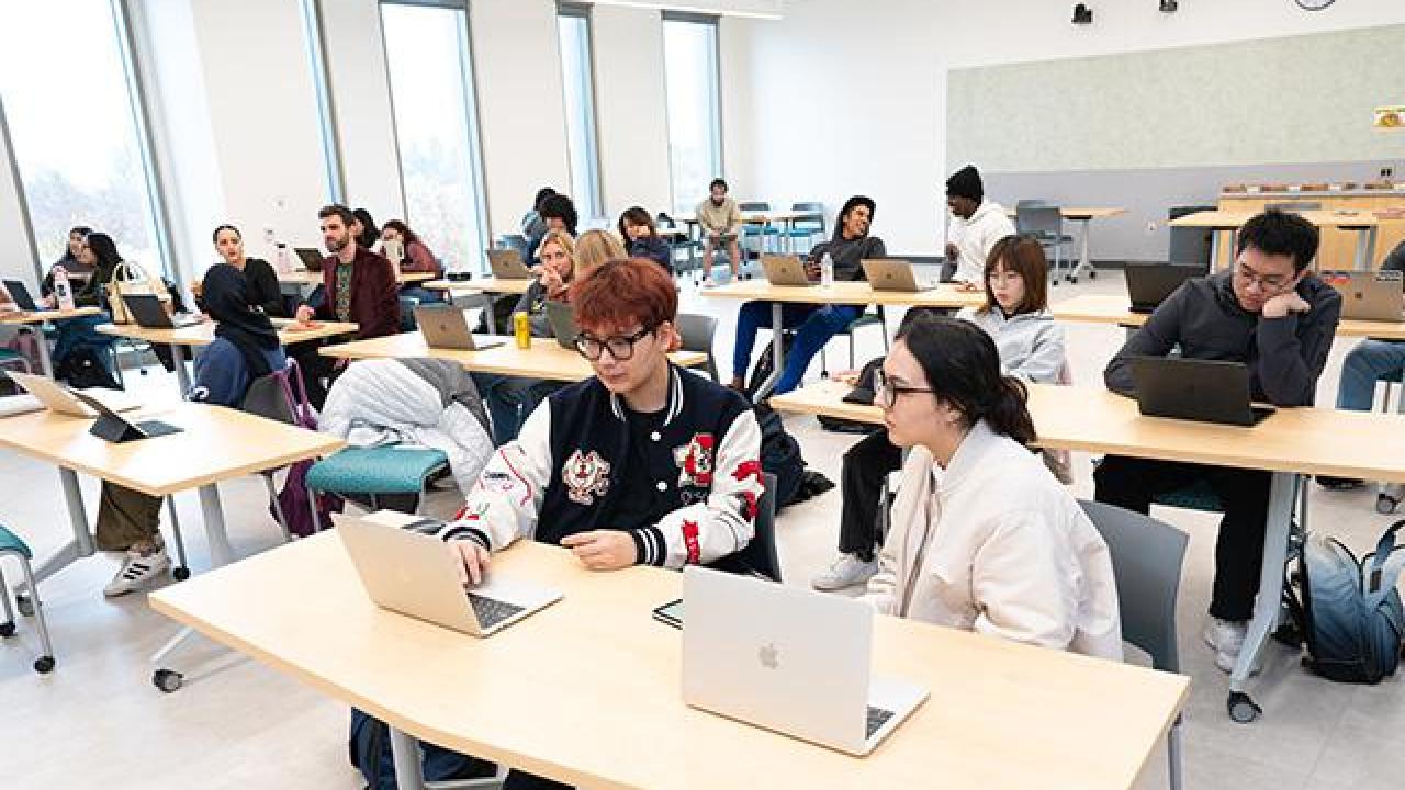 Writing Center large meeting area with students working in pairs at several long tables. 