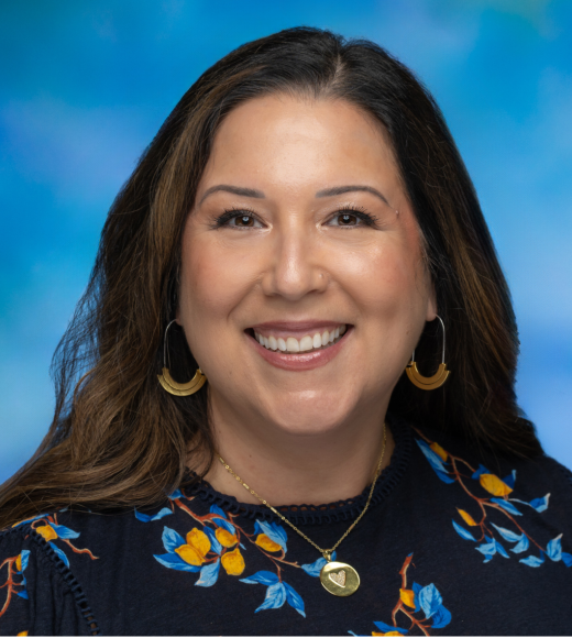 Picture of smiling Erica wearing a blue flowered top standing in front of a blue background.