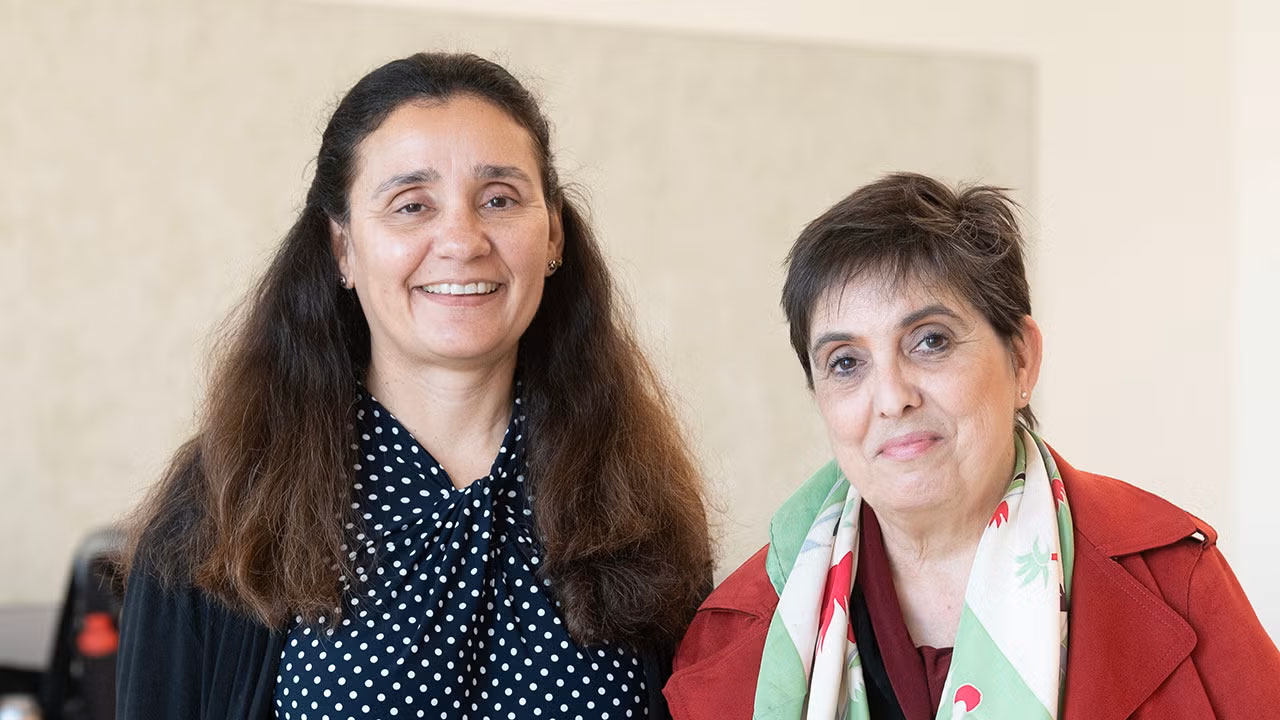 Two smiling women standing together, one in polka-dot blouse, one in red jacket and scarf
